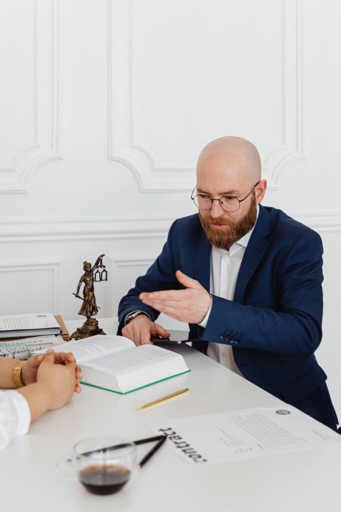 Man in suit consulting with client in elegant office, discussing documents on desk.